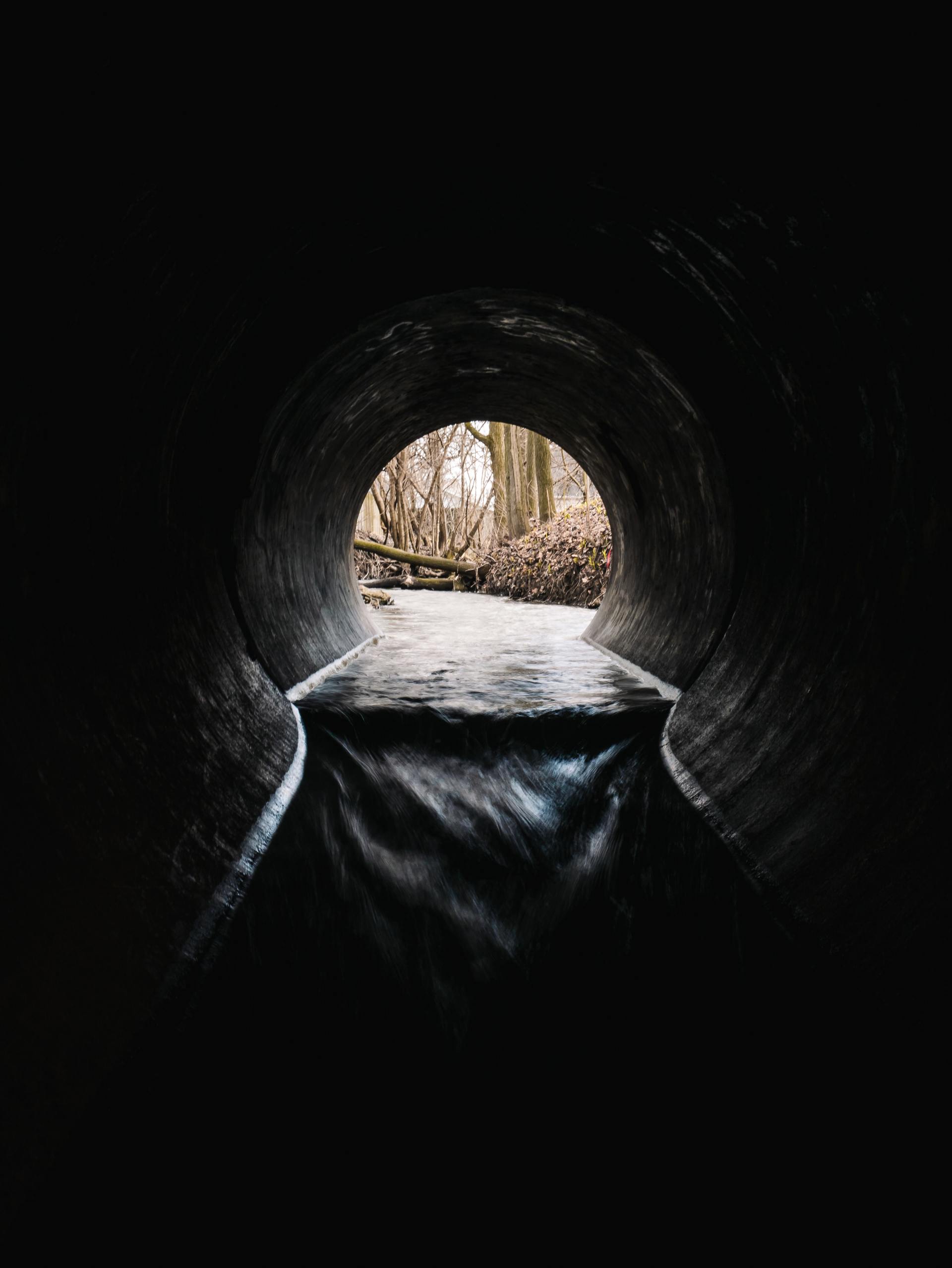 Tunnel opening to a forest scene; water flows out.