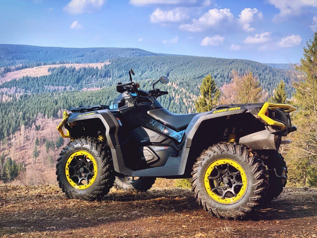 Un quad foncé avec des touches de jaune est garé à flanc de colline, surplombant une forêt.