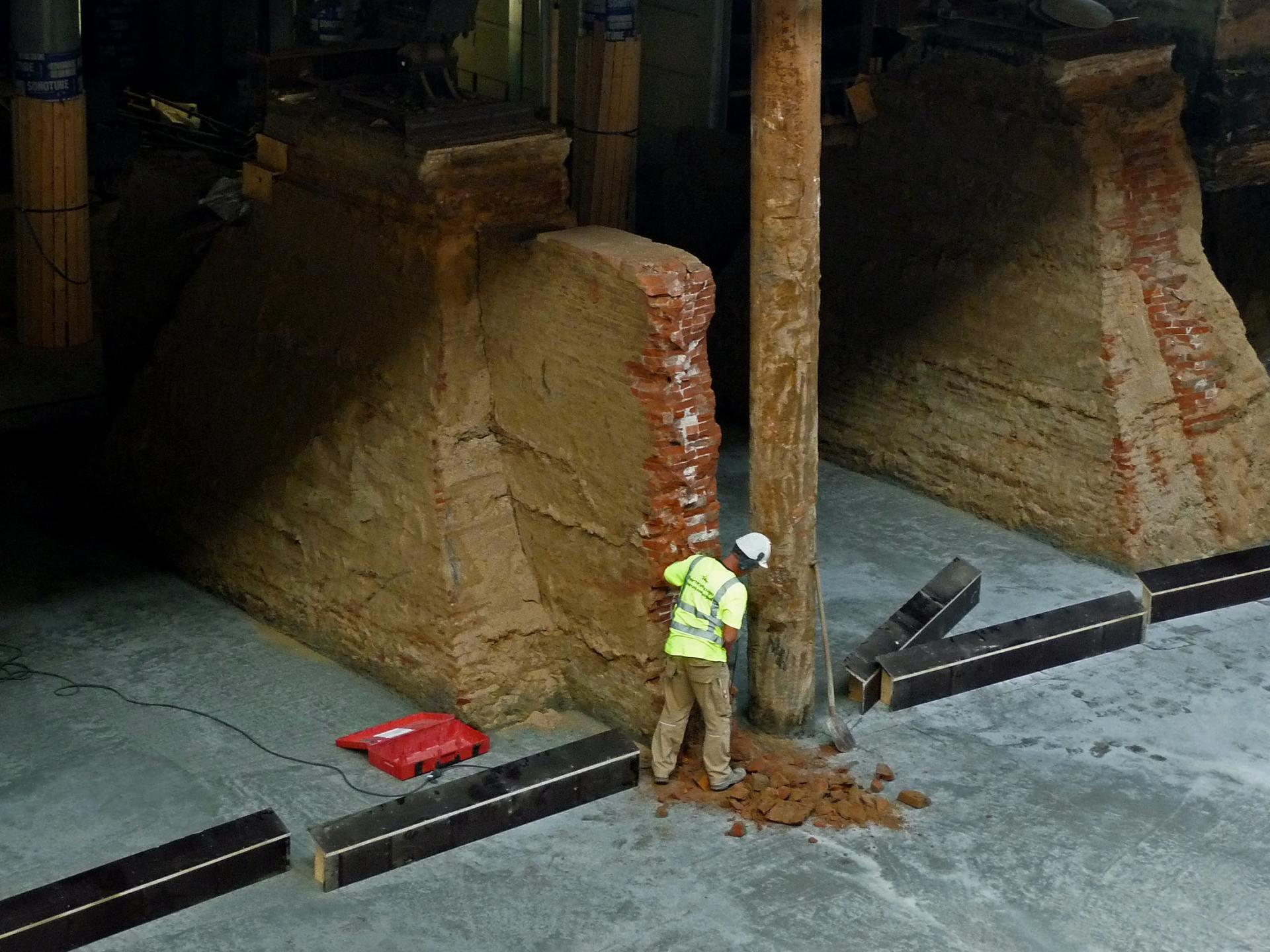 Worker in safety vest examines brick pillar in industrial setting.