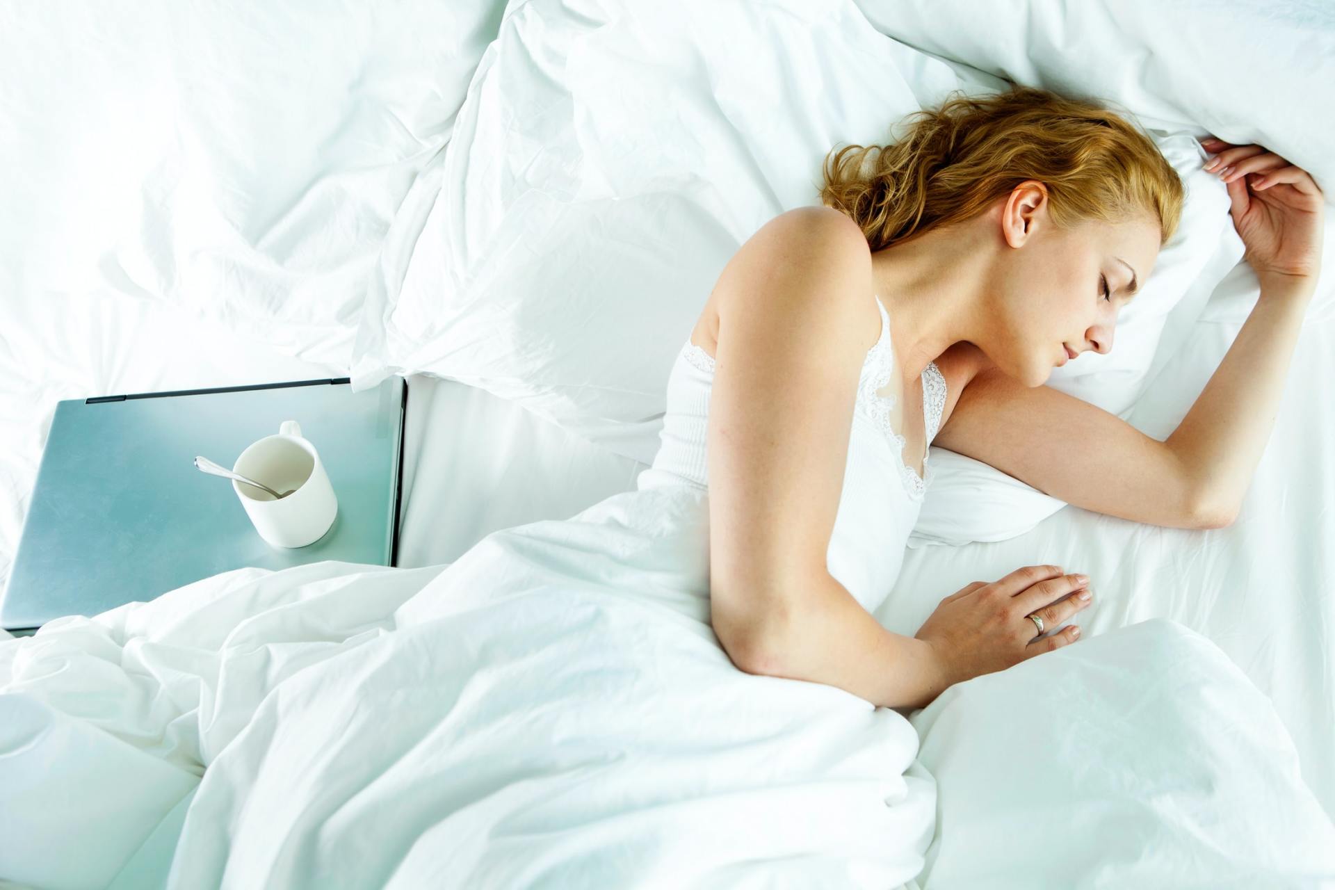 a woman is sleeping in a bed next to a laptop and a cup of coffee .