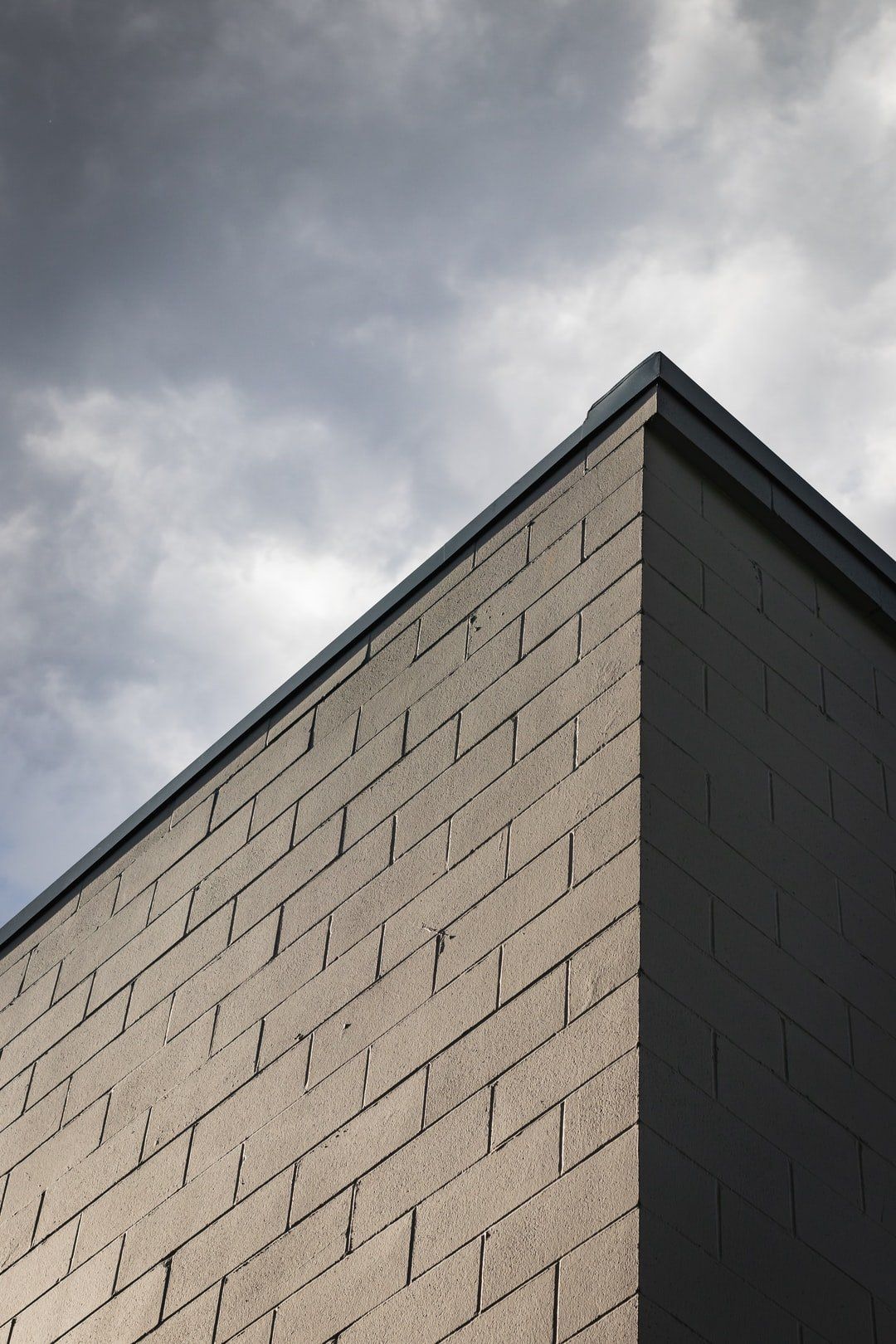 Corner of a dark brick building against a cloudy sky.