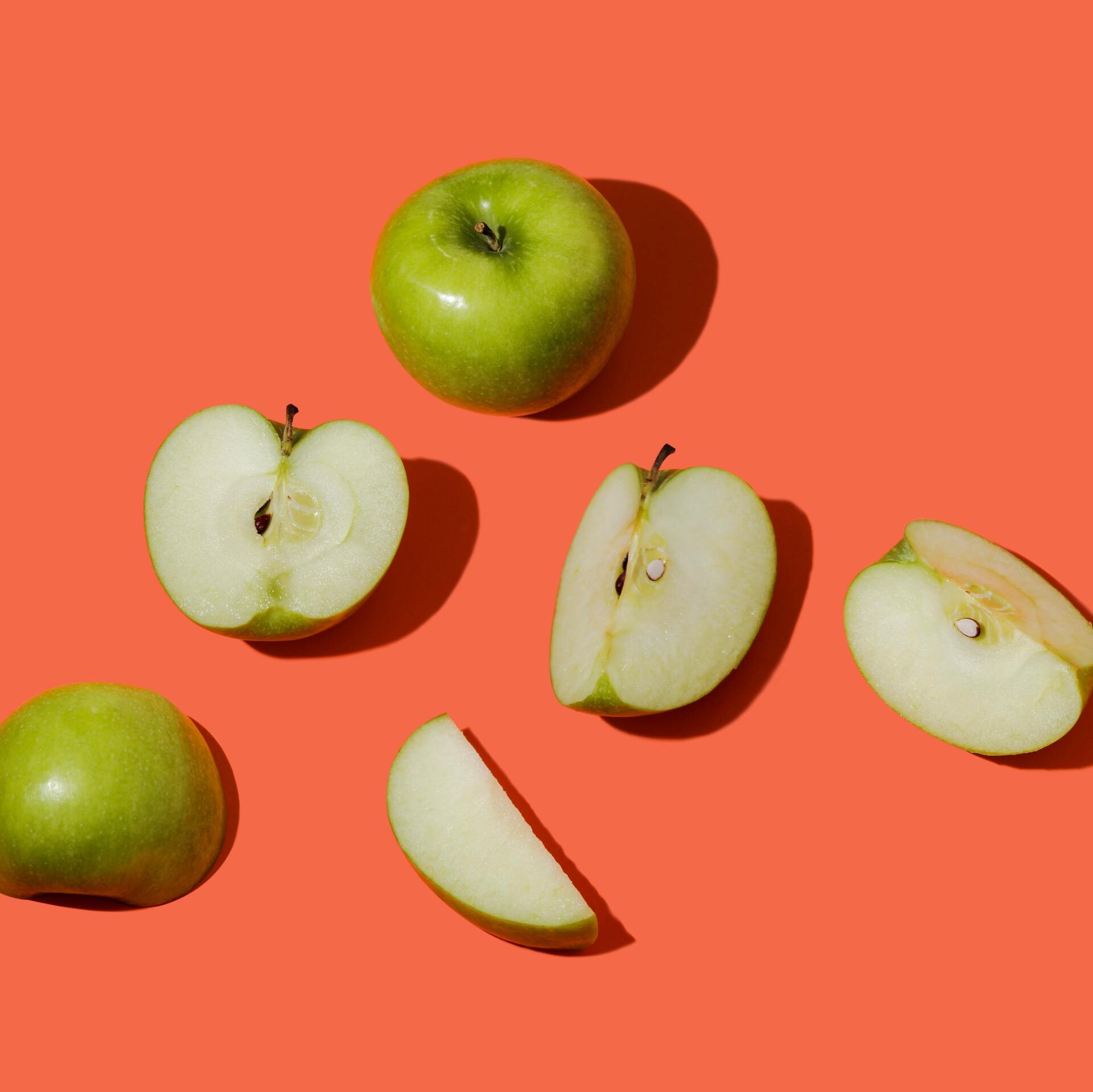 Green and sliced apples scattered on a coral background
