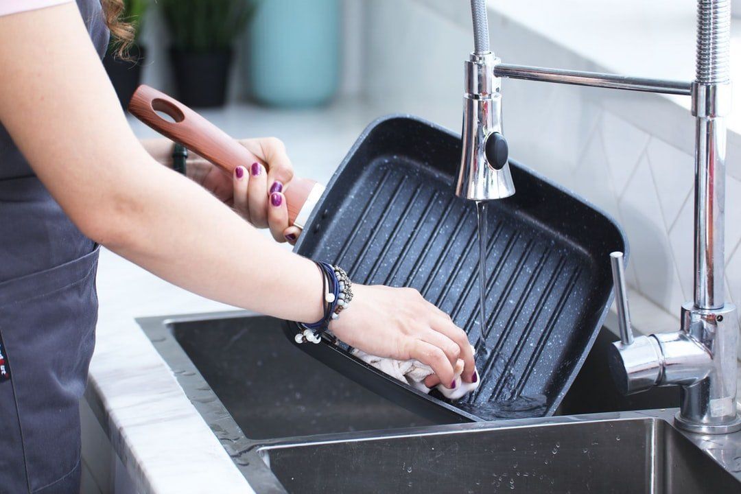 Woman washing a grill pan in a kitchen sink.