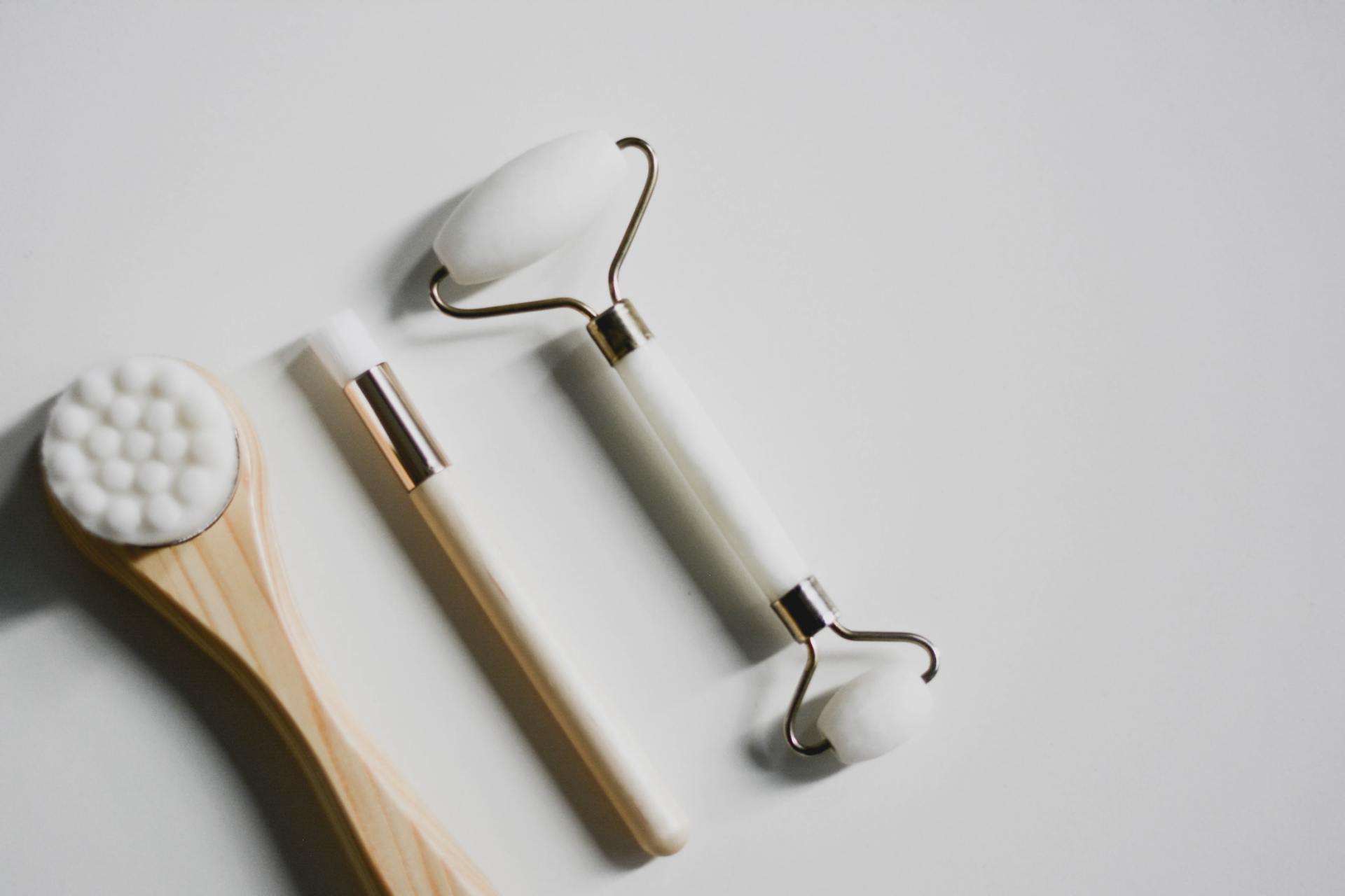 Wooden skincare tools and a jade roller on a light gray background