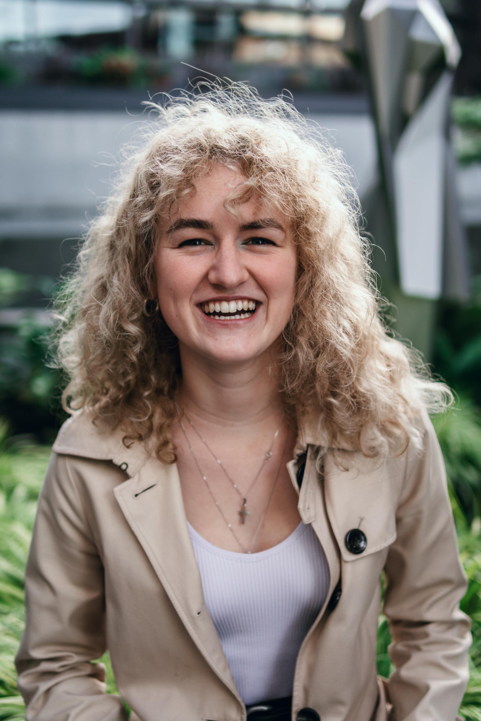 A woman with curly hair is smiling for the camera while wearing a trench coat.