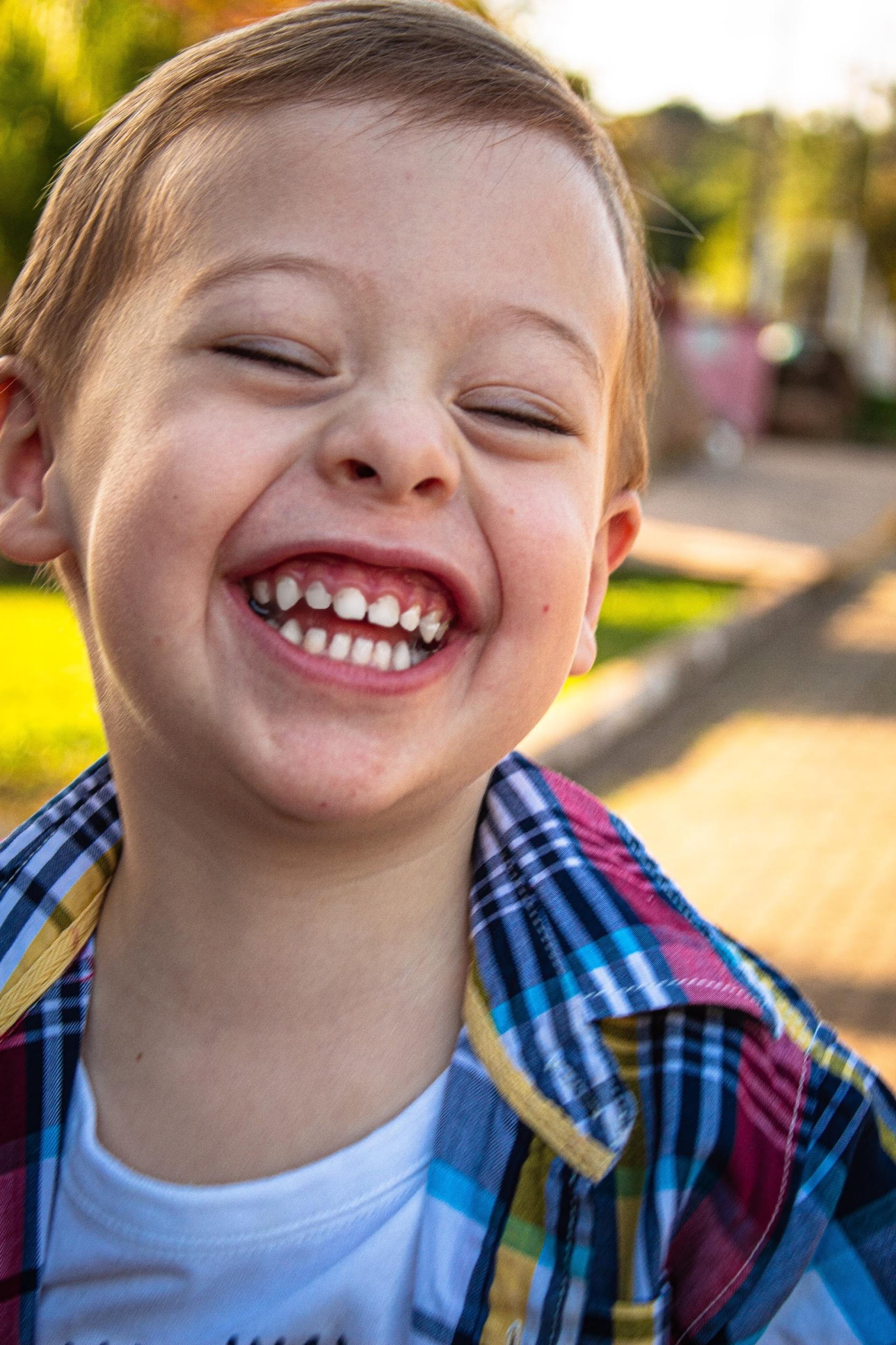 A young boy in a plaid shirt is laughing with his eyes closed.