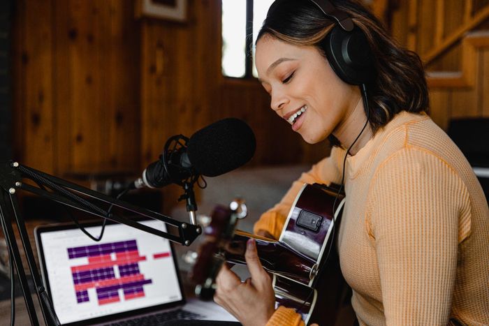A woman is playing a guitar in front of a microphone and a laptop.