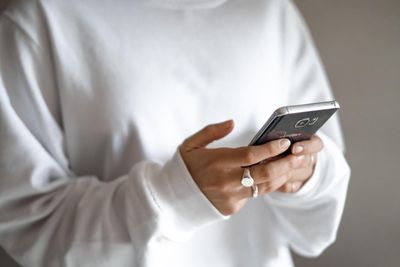 A person wearing a white sweater is holding a cell phone in their hands.