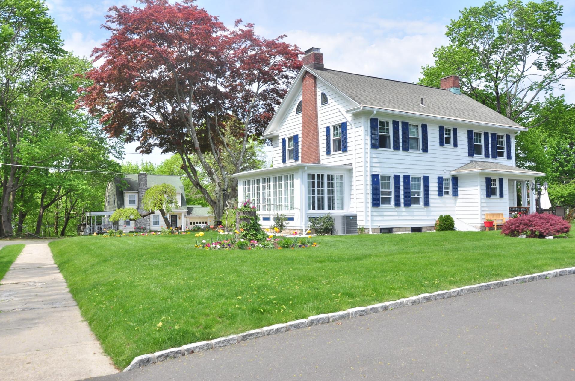 A white house with blue shutters sits on a lush green lawn