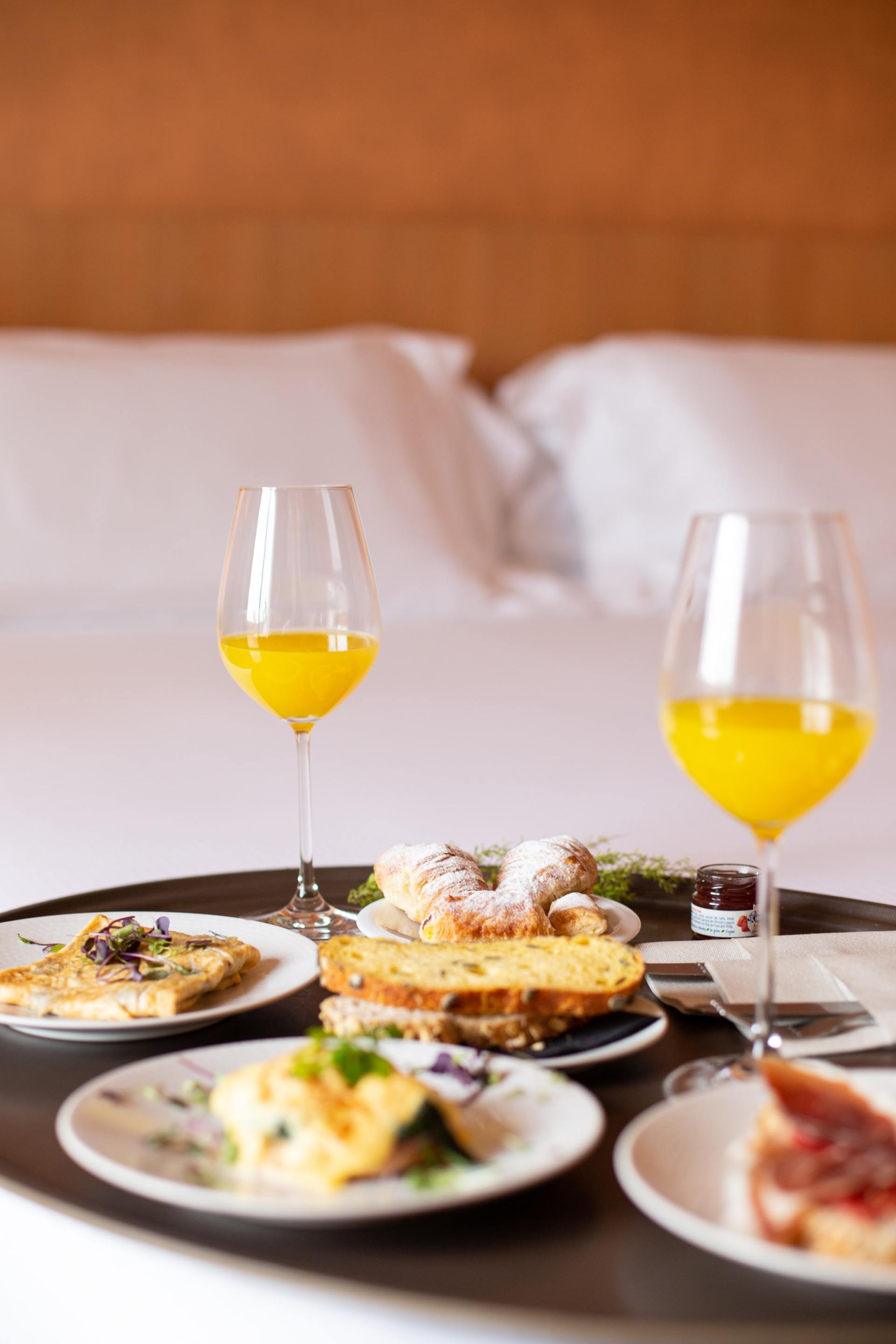 A tray of food and wine glasses on a bed