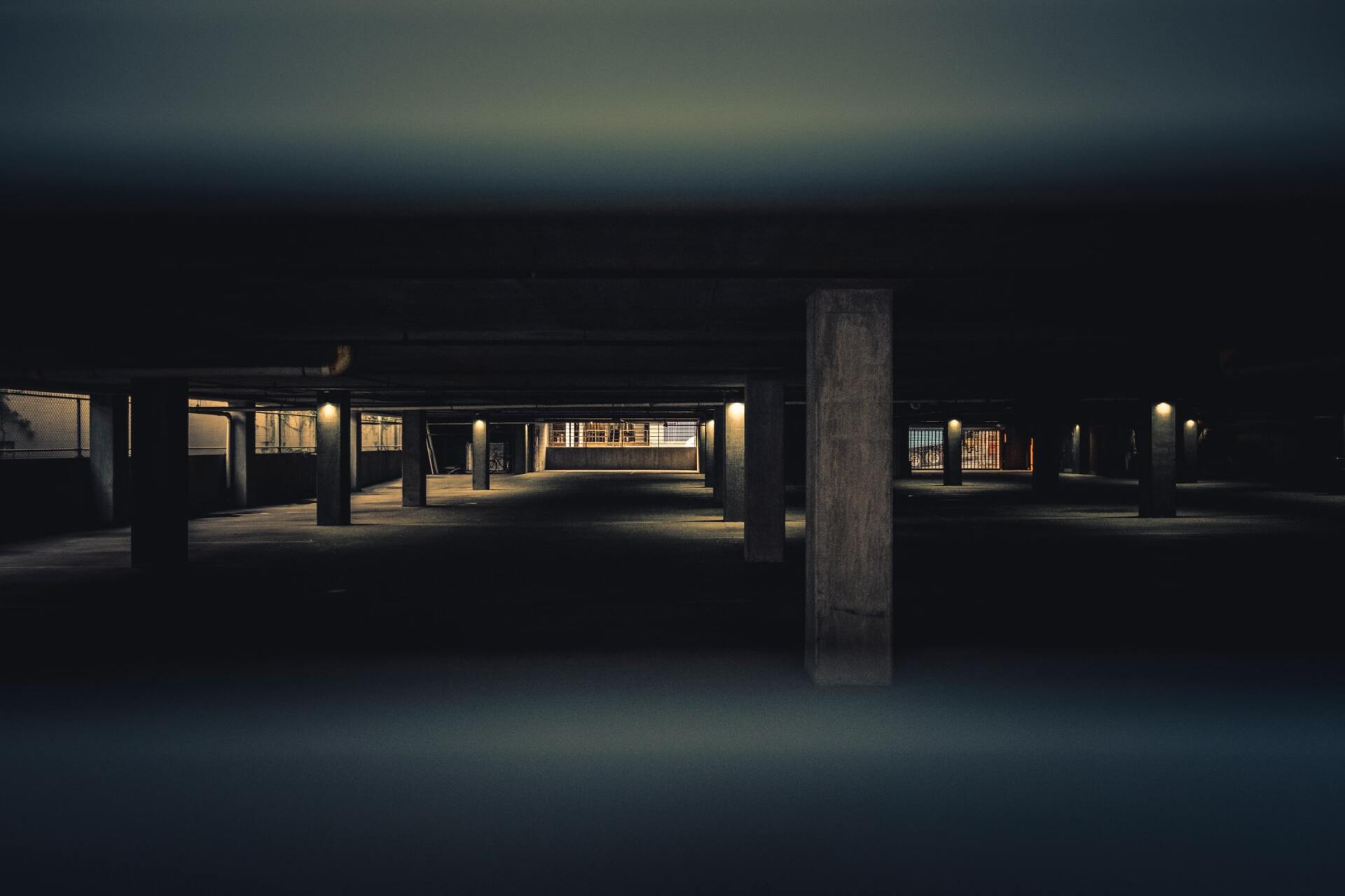 Dark, empty arcade lit by interior lights. Columns frame the space, with a dim glow at the far end.