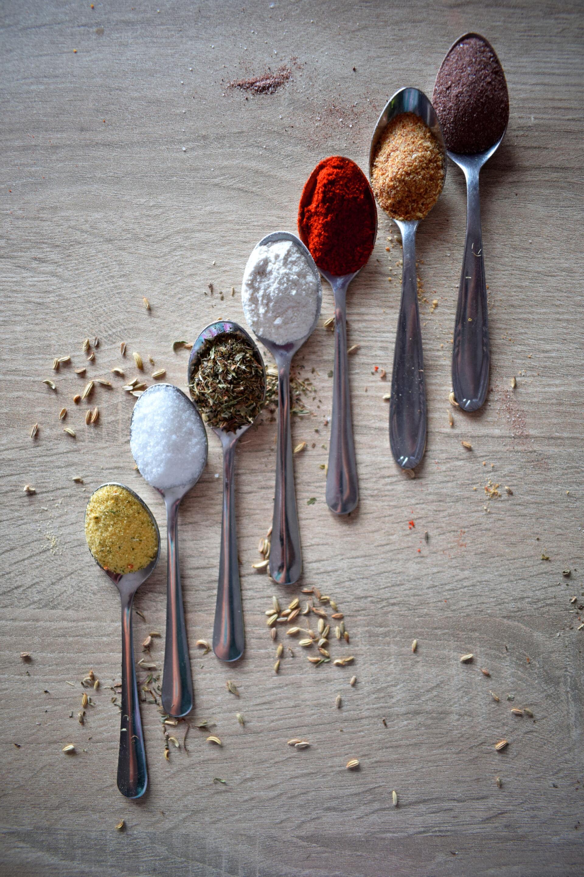 A wooden table topped with spoons filled with different types of spices.