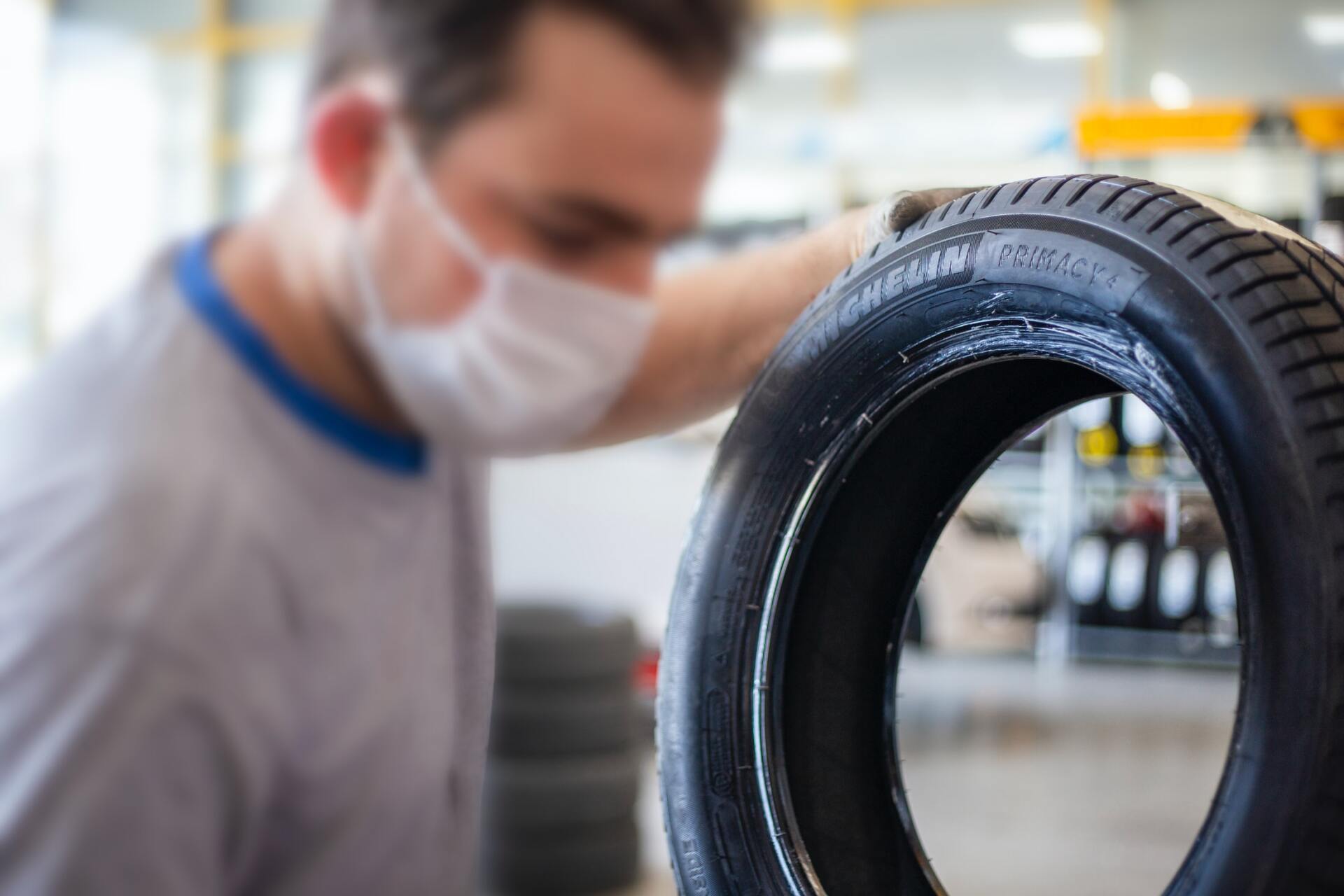 Mechanic wearing a mask inspecting a tire in a garage, possibly for repair.
