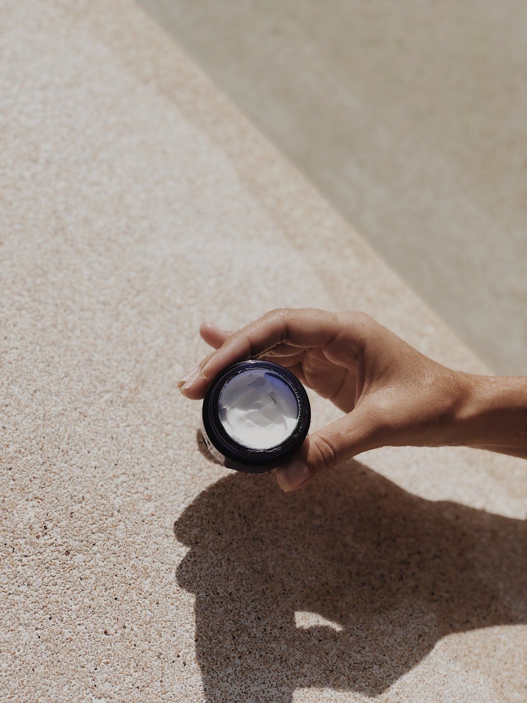 Hand holding a small round lens over a sunlit textured surface, casting a shadow