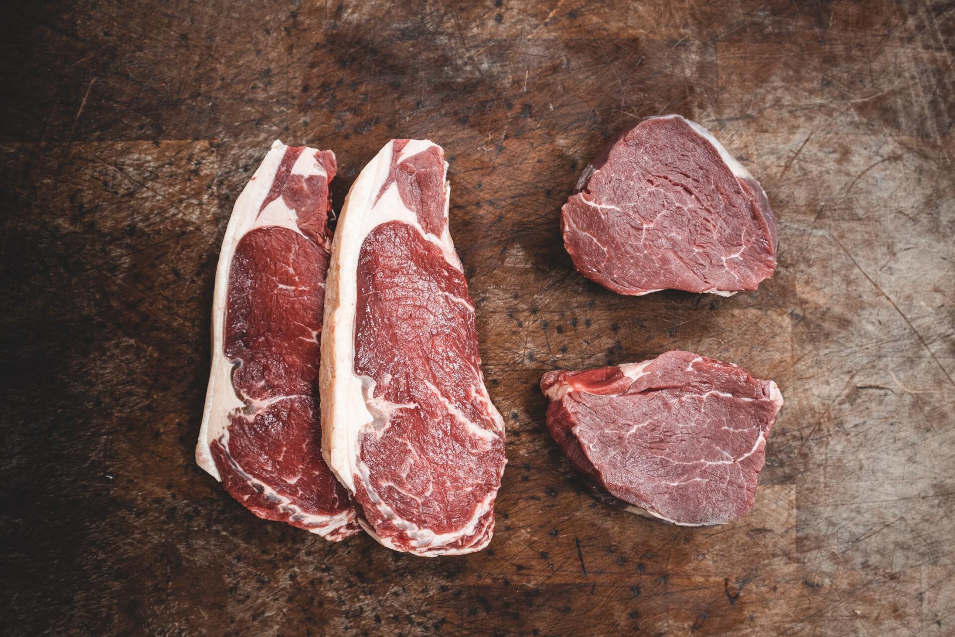 Three pieces of raw beef are sitting on a wooden table.