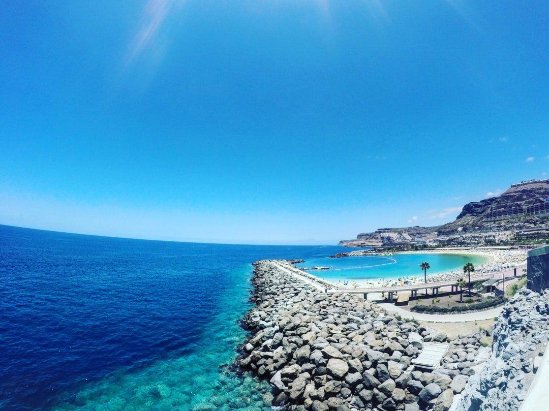 Ein von Felsen und Wasser umgebener Strand an einem sonnigen Tag.