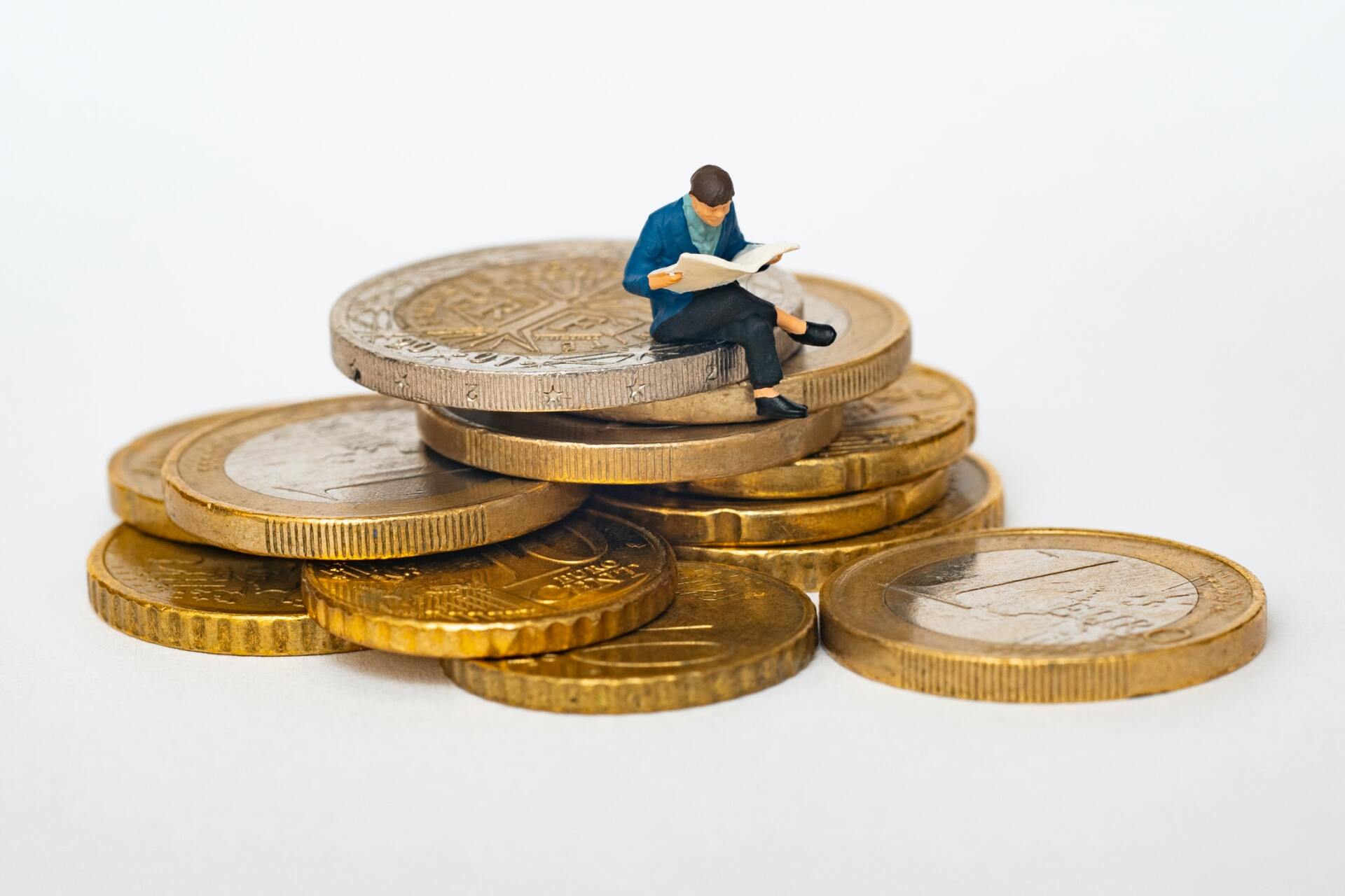 Eine Miniaturfigur liest eine Zeitung auf einem Stapel Euro-Münzen.