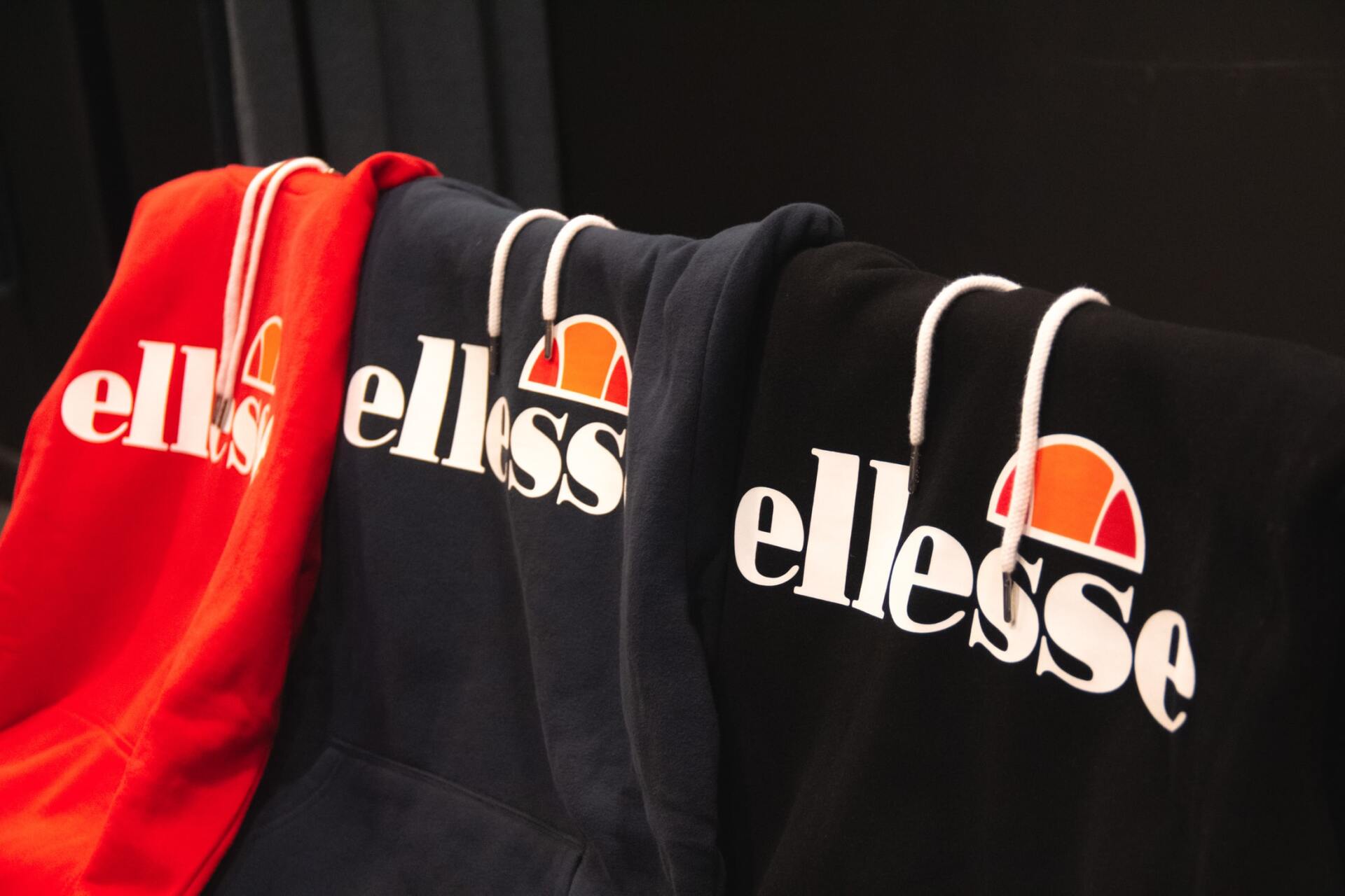 Ellesse hoodies in red, navy, and black hanging on a clothing rack