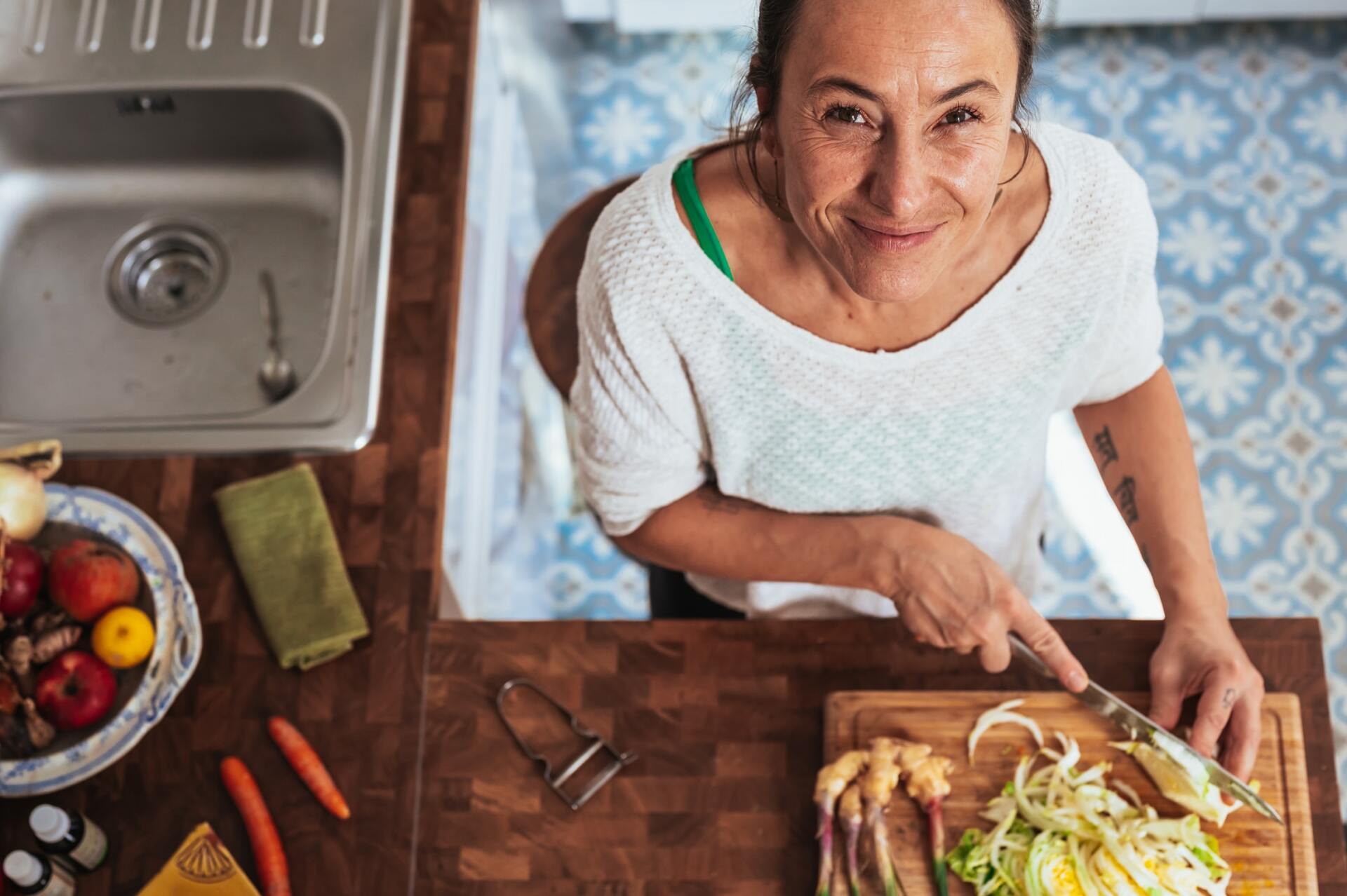 A woman is cutting vegetables on a cutting board in a kitchen.