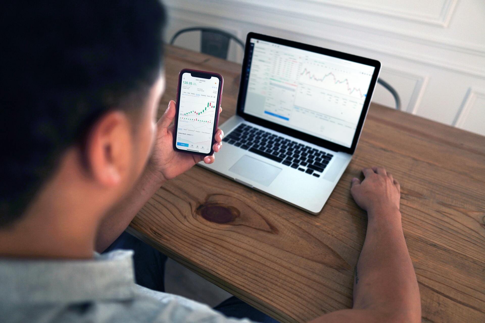 Um homem está sentado a uma mesa usando um laptop e um telefone celular.