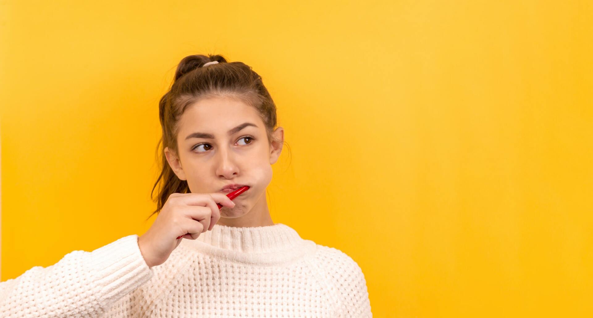 A young woman in a white sweater is eating a red lollipop.