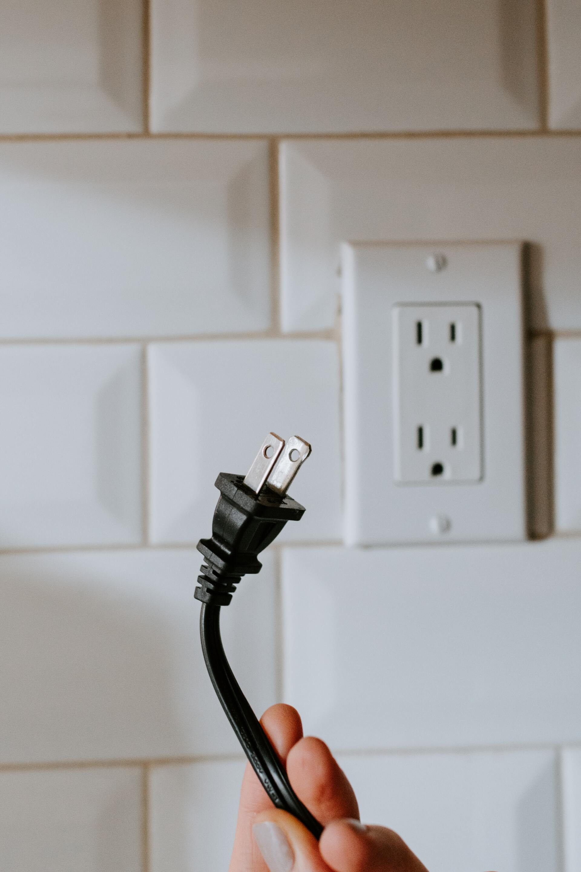 Main tenant une prise électrique noire à côté d'une prise murale blanche.