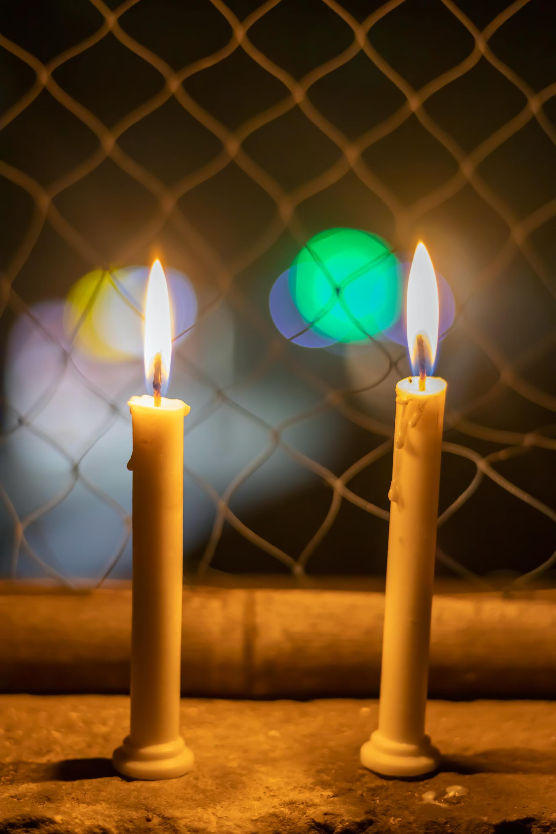 שני נרות דולקים מול גדר רשת.