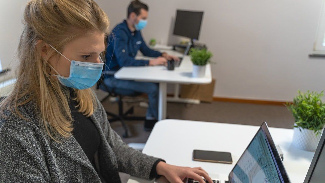 A woman wearing a face mask is using a laptop computer in an office.