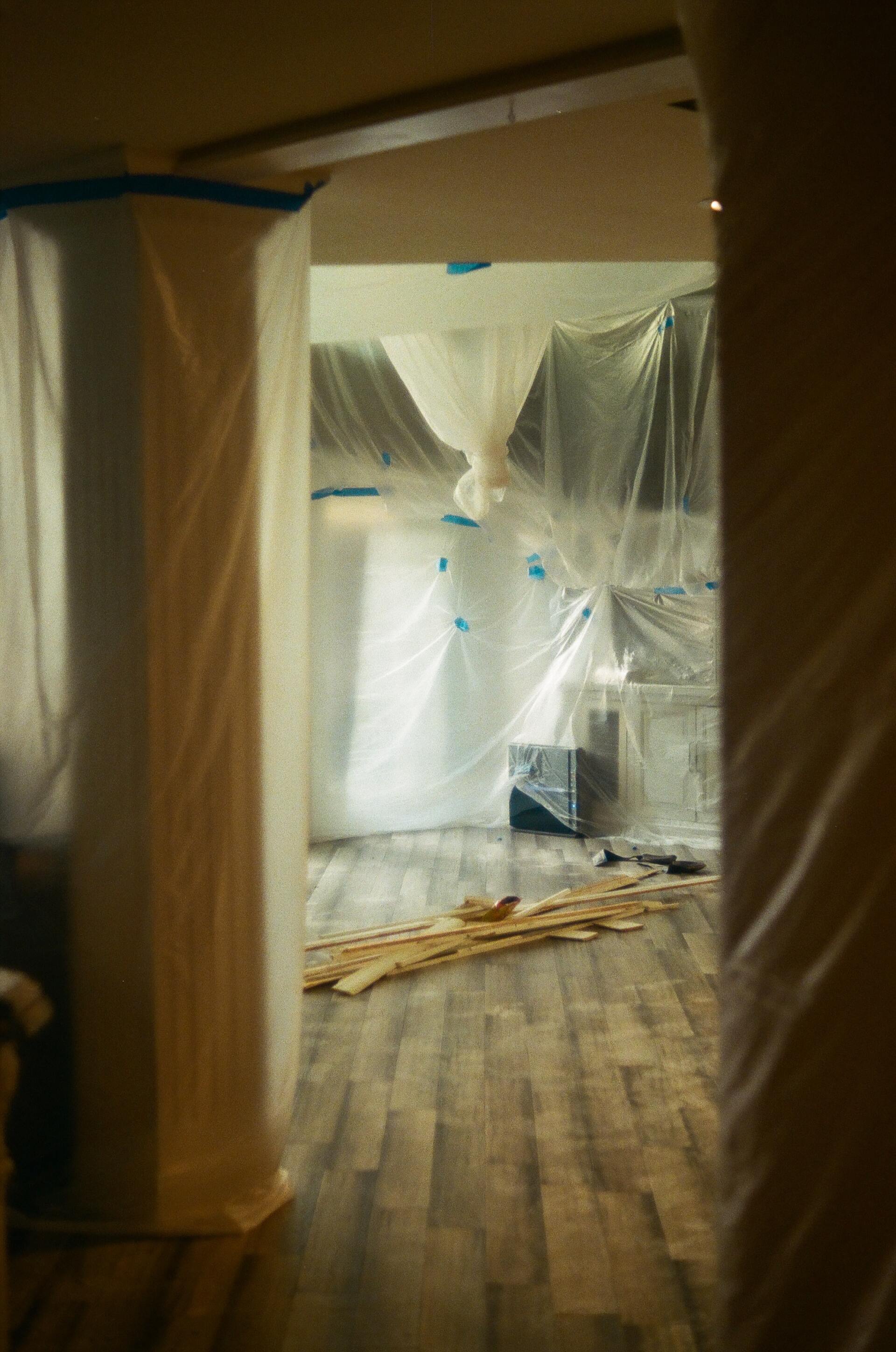 Room under construction, covered in plastic sheeting, with exposed flooring and wood planks.