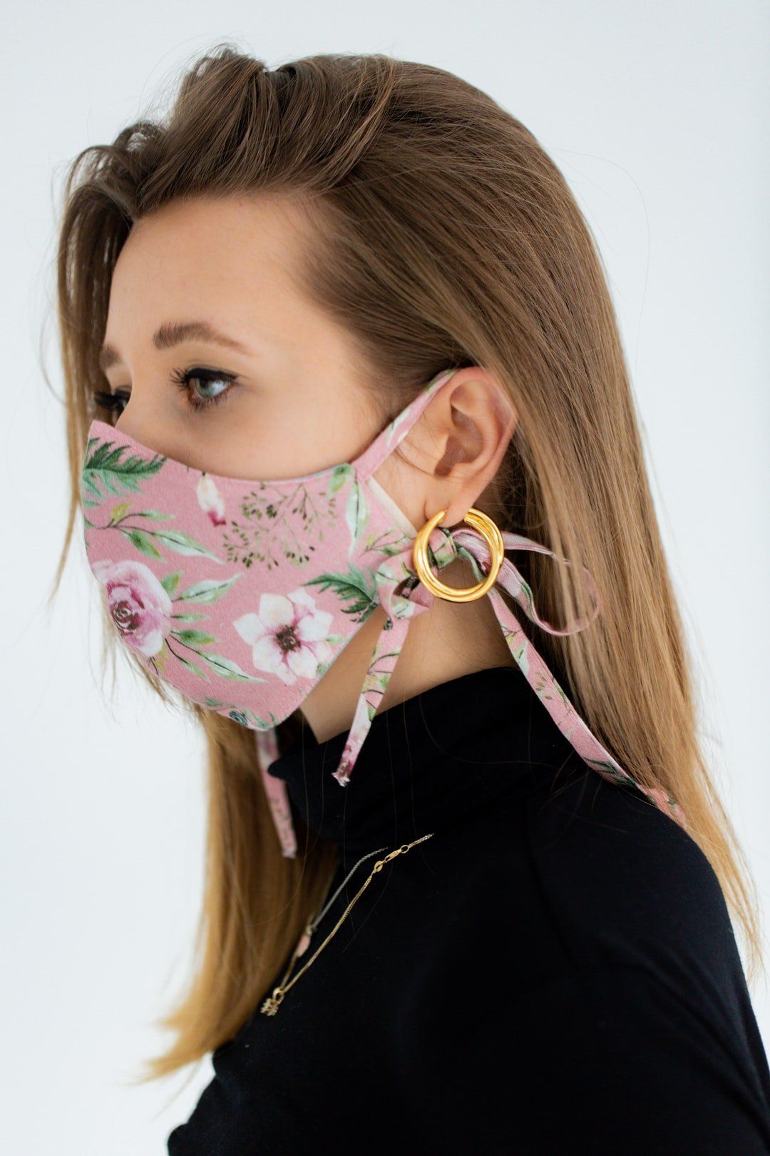 A woman wearing a pink floral face mask and earrings.