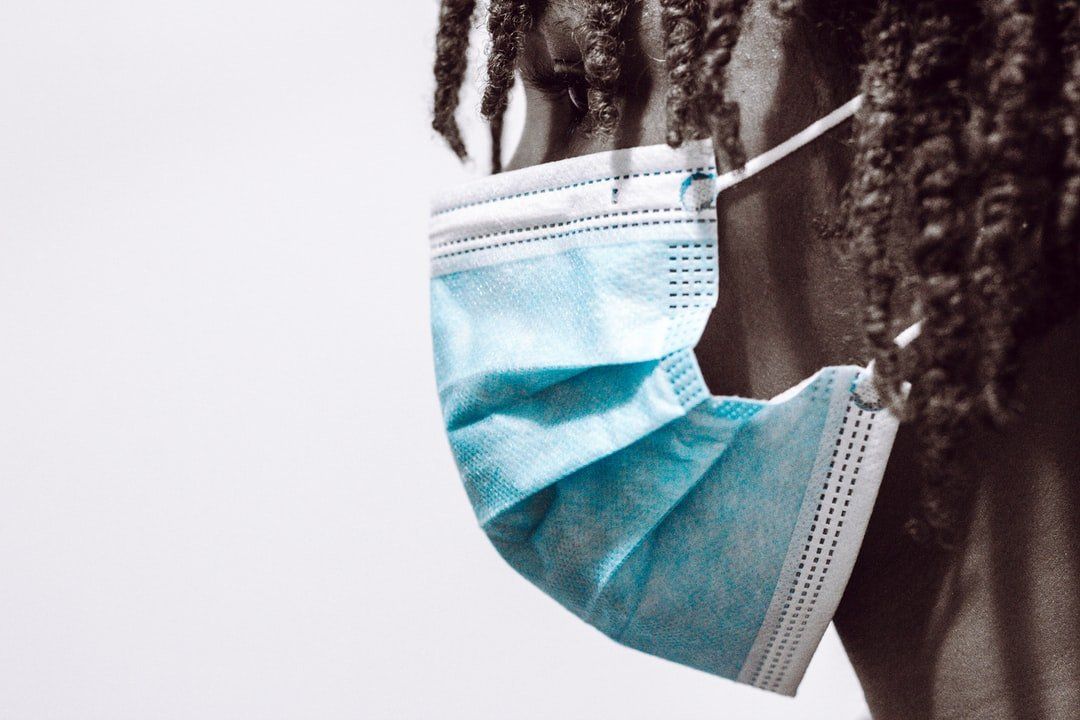 A person with dreadlocks is wearing a blue face mask.