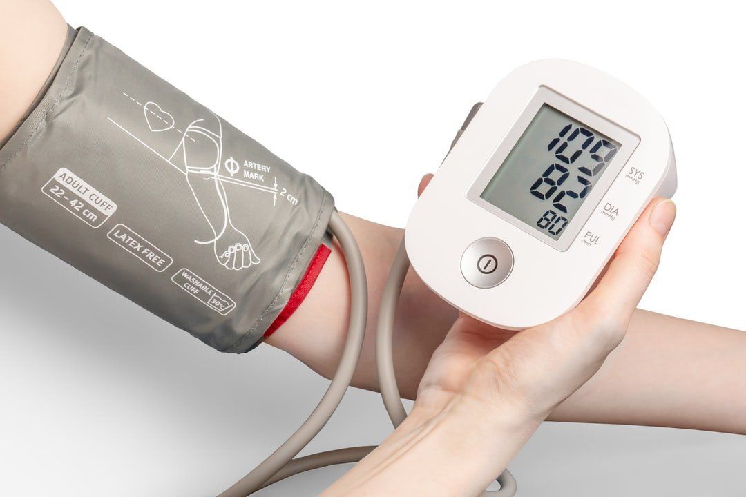 Person taking blood pressure with a digital monitor; arm with cuff, display shows 109/69.