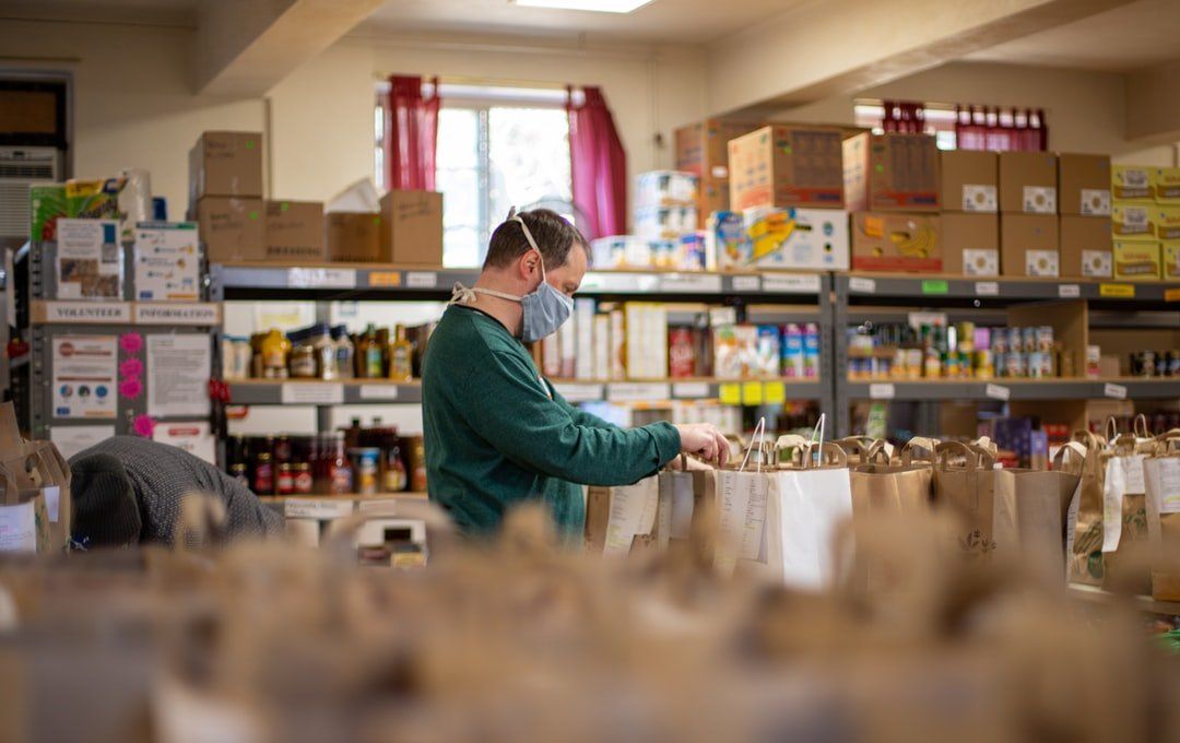 A man wearing a mask is standing in a room filled with bags of food.