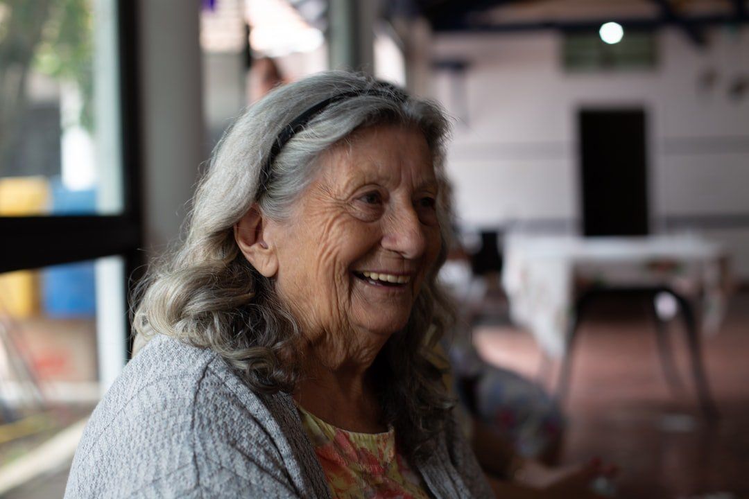 A close up of an elderly woman smiling in a room.