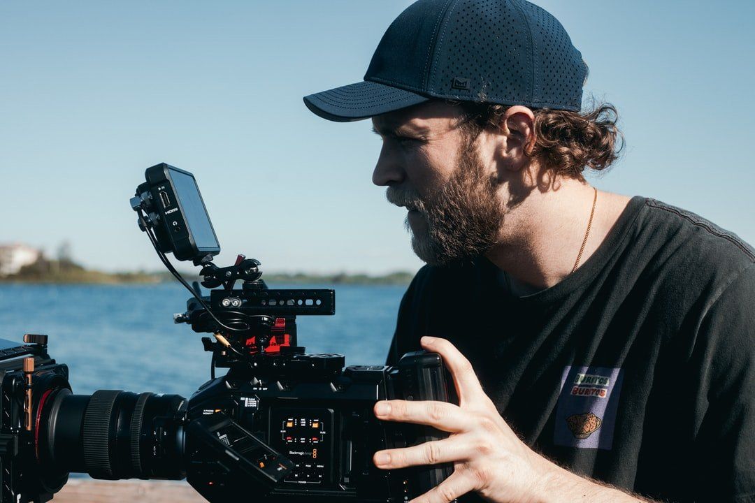 camera man in blue hat filming next to water