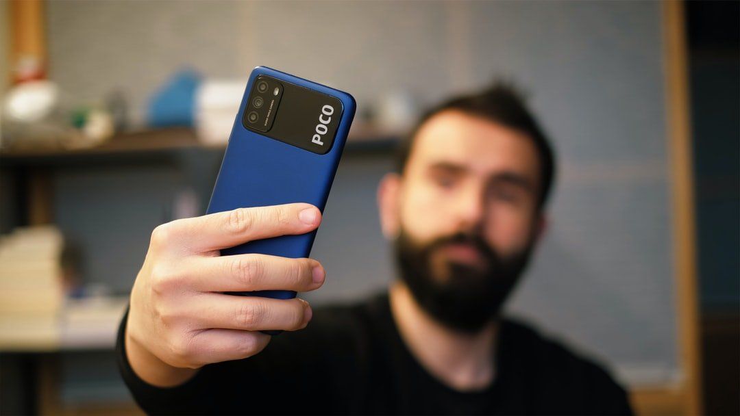A man with a beard is taking a selfie with his phone.