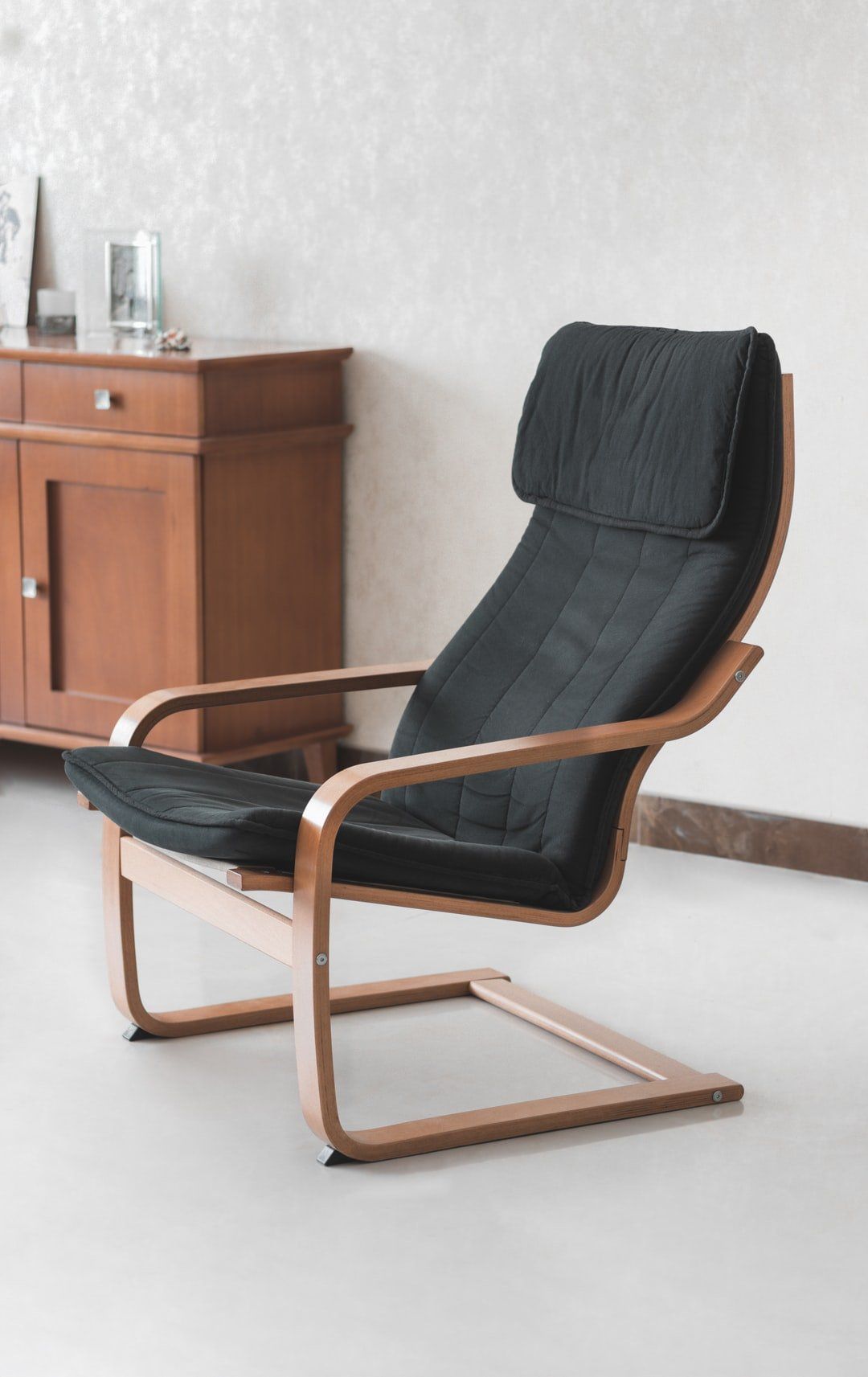 A black chair is sitting in a living room next to a wooden cabinet.
