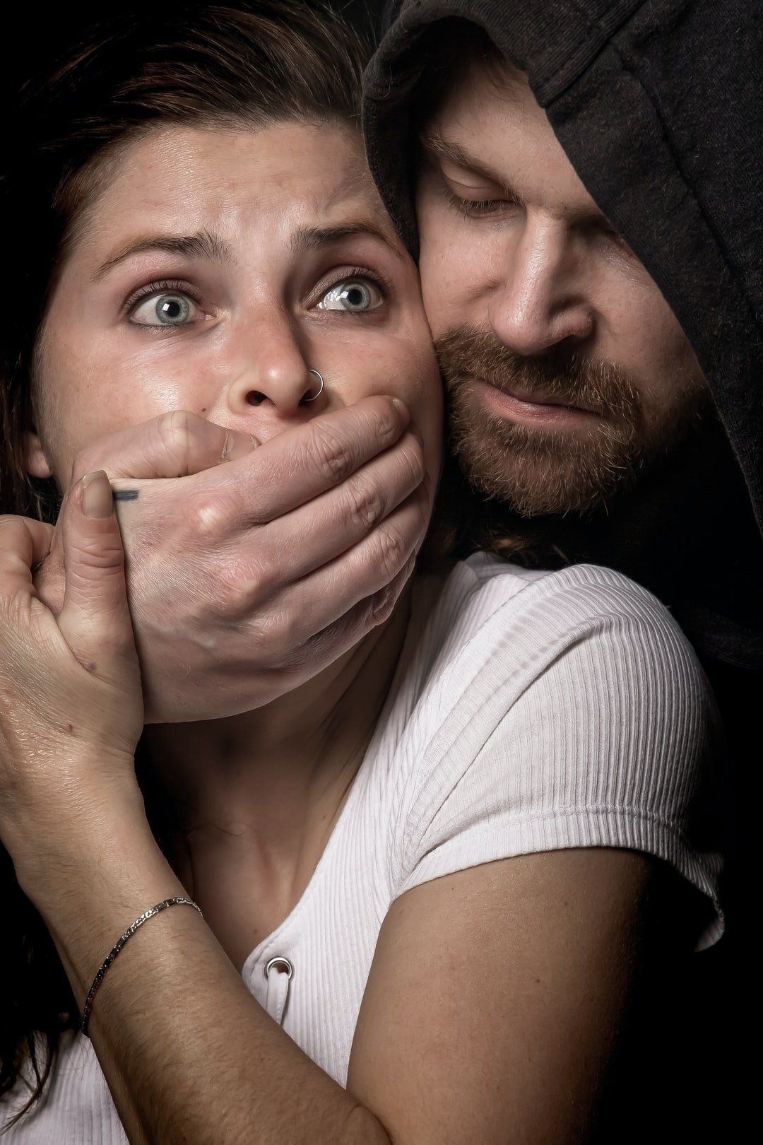 Woman with panicked expression, hand over her mouth as man in a hoodie looms over her.