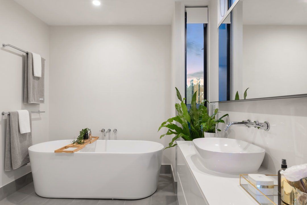 Modern white bathroom with a free-standing tub, vessel sink, and greenery.