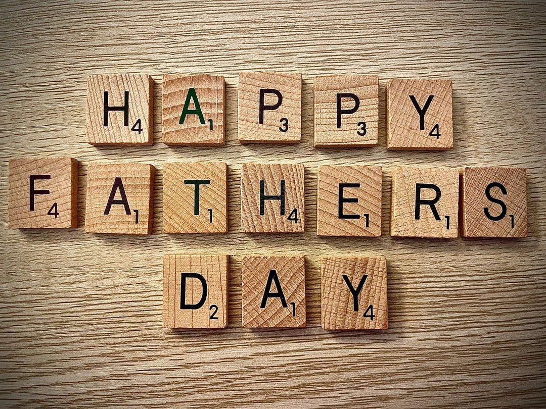 Happy father 's day is written in scrabble tiles on a wooden table.